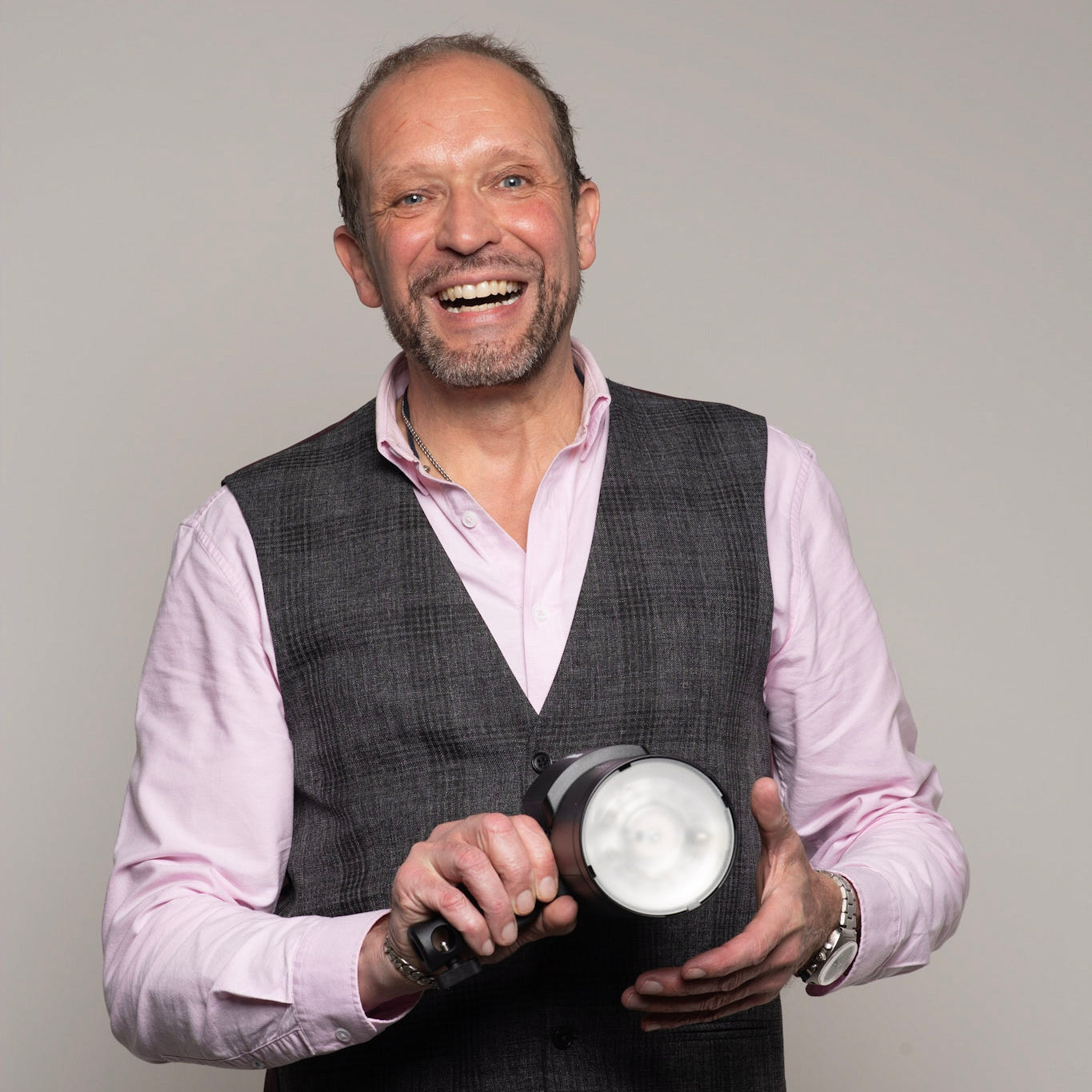 Tourso image of AJ's director and proprietor holding a Profoto B10X, wearing a wasit coat and pink shirt.