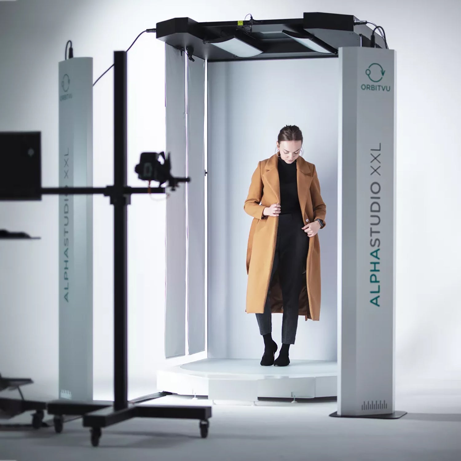 Female model in the Alphastudio XXL automated photo video studio system with a camera in the foreground, on a white background.