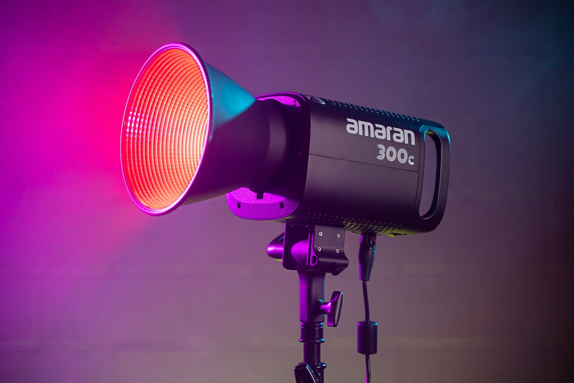 Amaran 300c LED CoB Light with Bowens Mount Hyper Reflector attached alongside pink lighting.