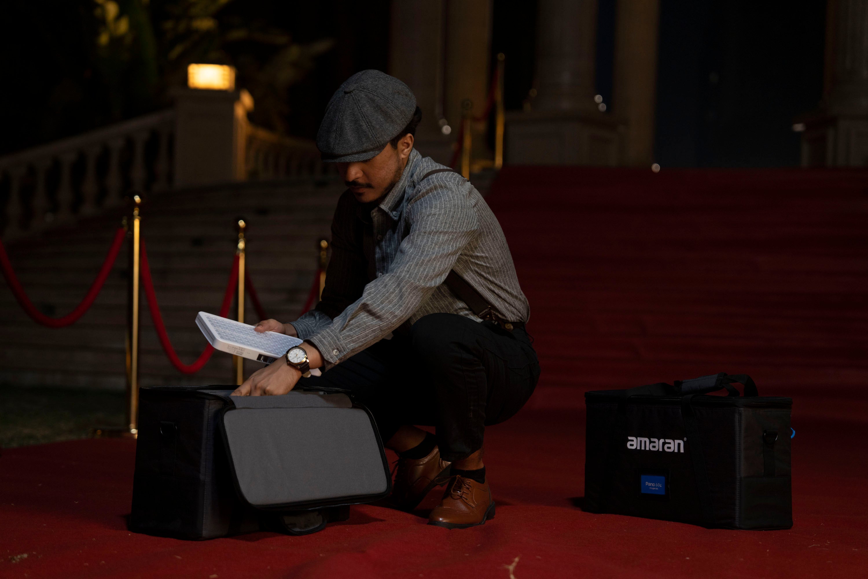 Person holding an amaran Pano 60c Light Panel, with two carrying bag's pictured on a red carpet.