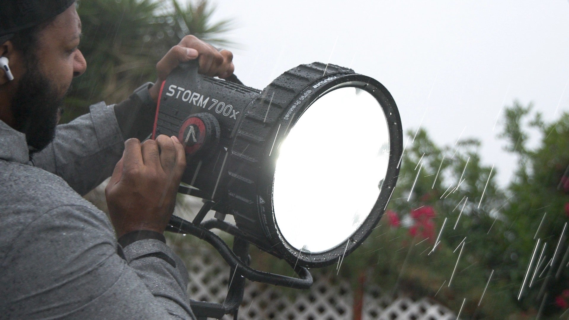 Person holding a large LED fixture labeled 'STORM 700x' outdoors on a rainy day.