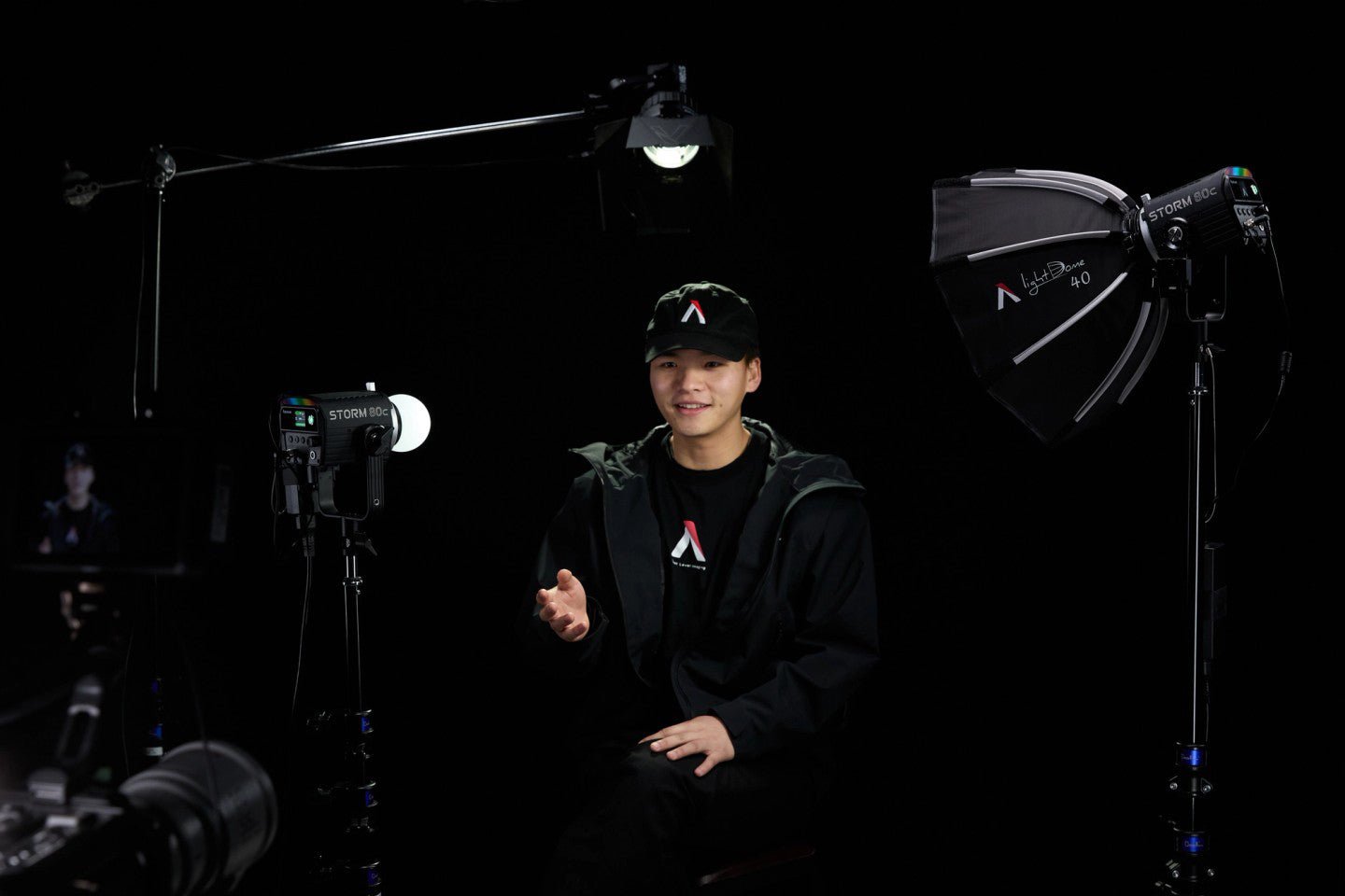 Person in a dark room with the Storm 80c Three Head Kit set up as an interview scene. The lights are on stand and the top light is on a boom.