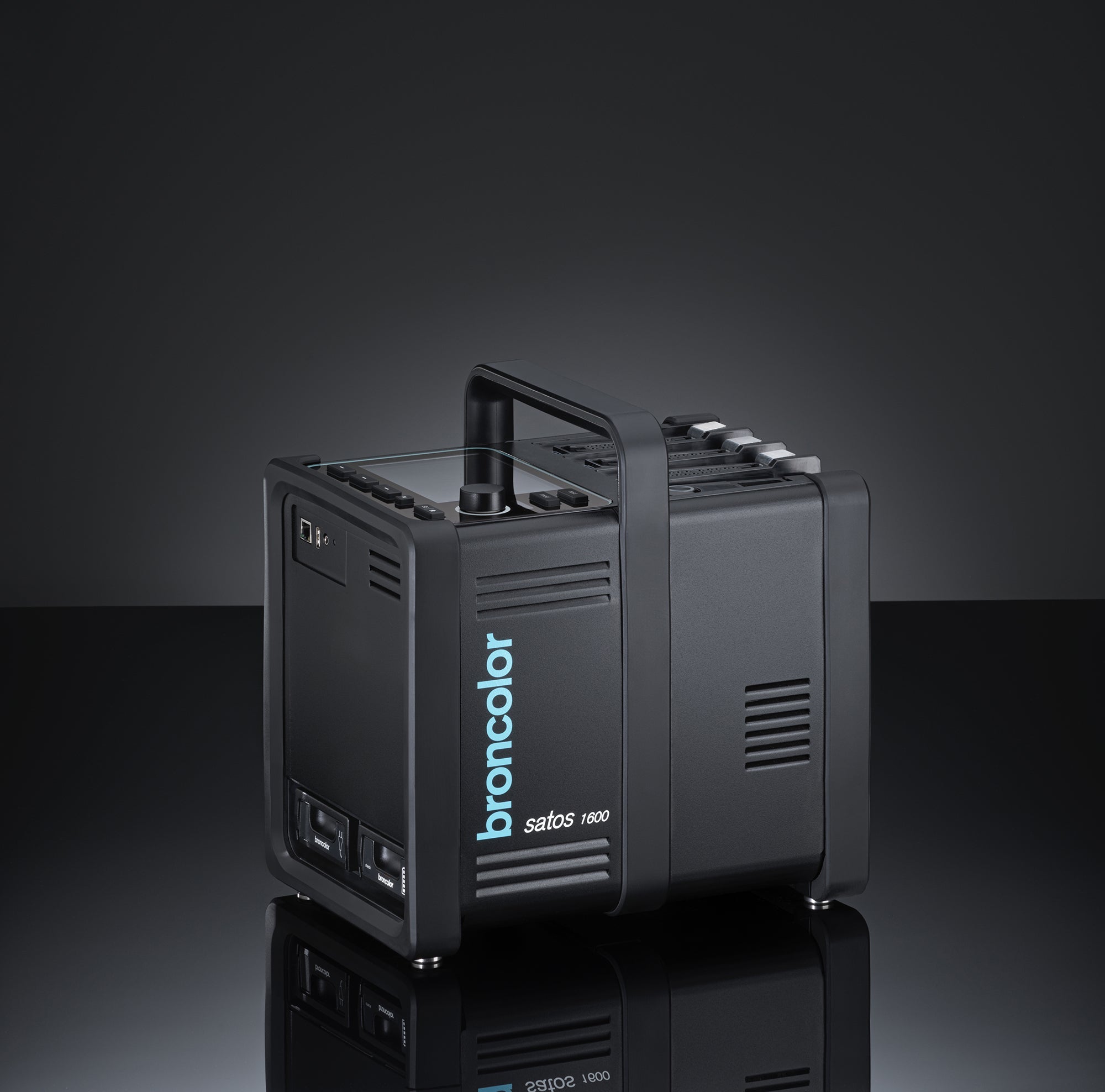 A black Broncolor Satos 1600J power pack for flash lighting, featuring a handle and various control buttons and displays.
