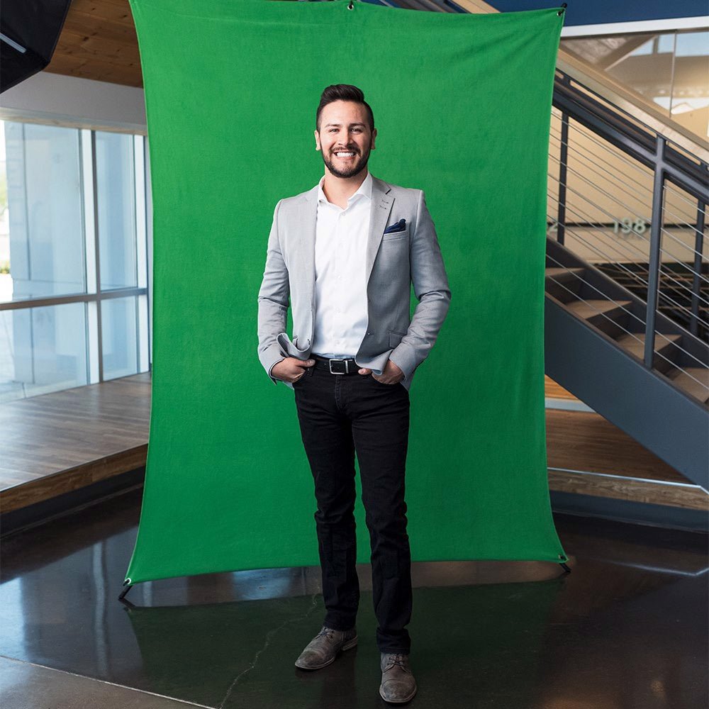 Wide shot of a smiling happy man photographed against a green fabric stretch background, shown in a modern rooftop scene.