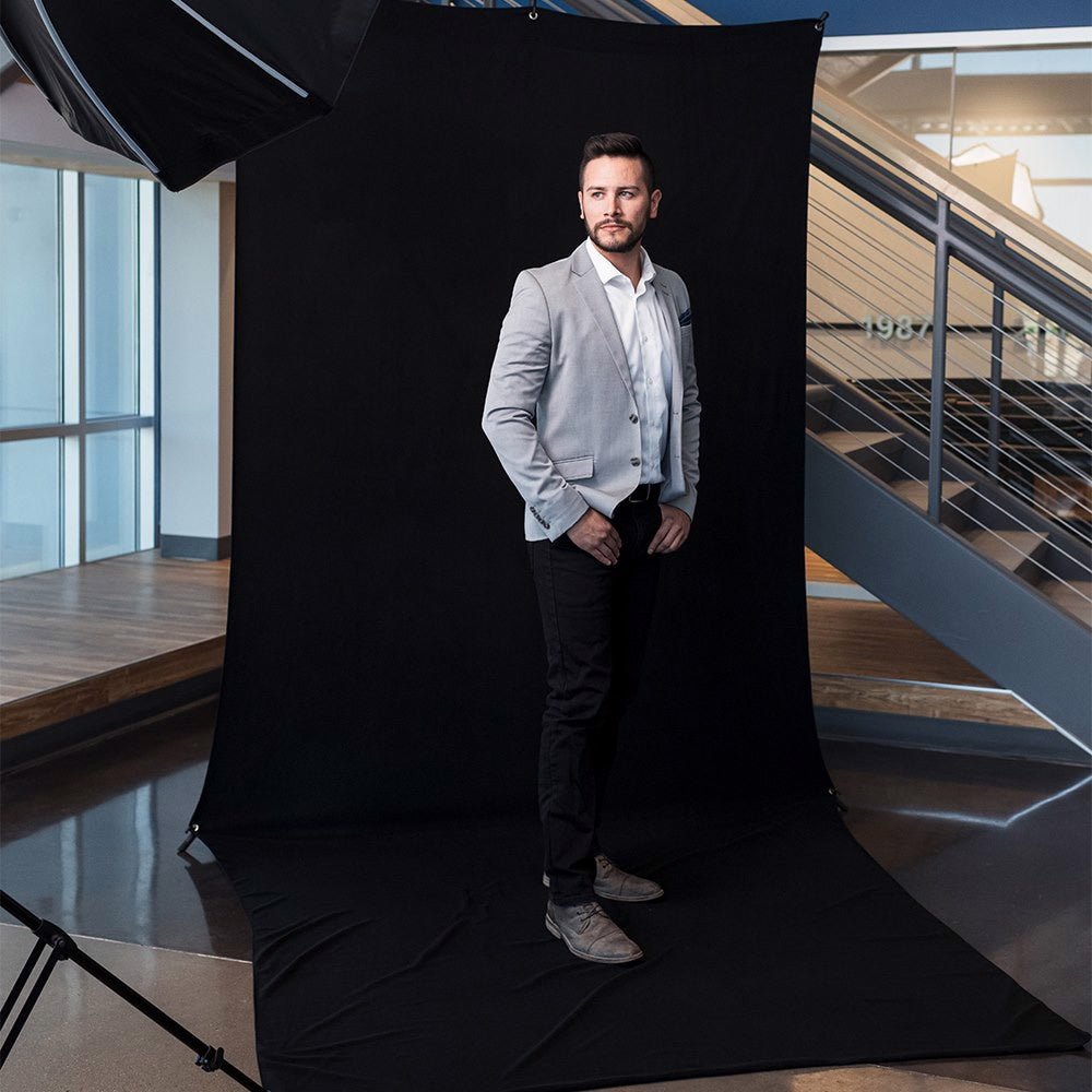 Gentleman shown being photographed against a fiull lenght black semaless fabric background in a rooftop city scene with blue sky.