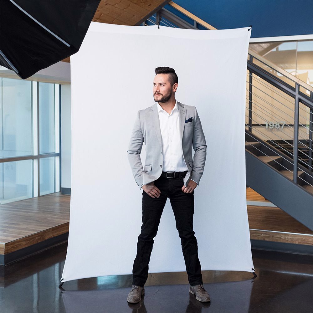 Wide shot of a man photographed against a white fabric strech background, shown in a modern rooftop scene.
