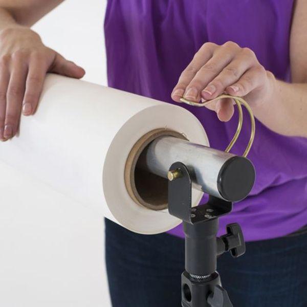 A person pictured attaching a roll of background paper to the Colorama Solo Background Support 4m (13ft) Heavy Duty.