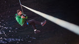 A Profoto photographer suspended on a zip line over the sea, poised ready and waiting to take photos of rock climbers