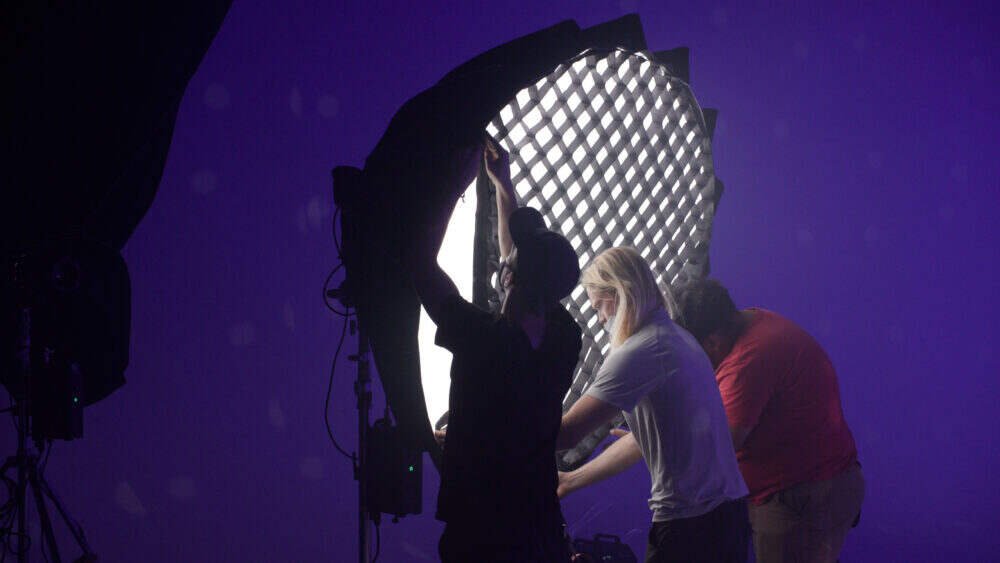 Aputure softbox with technicians applying a honeycomb grid on set.