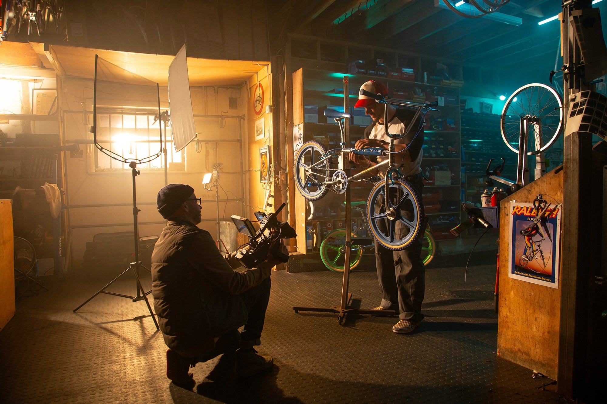 Inside a bike repair shop, showing a lighting technician setting up the shot of a technician working on the BMX.