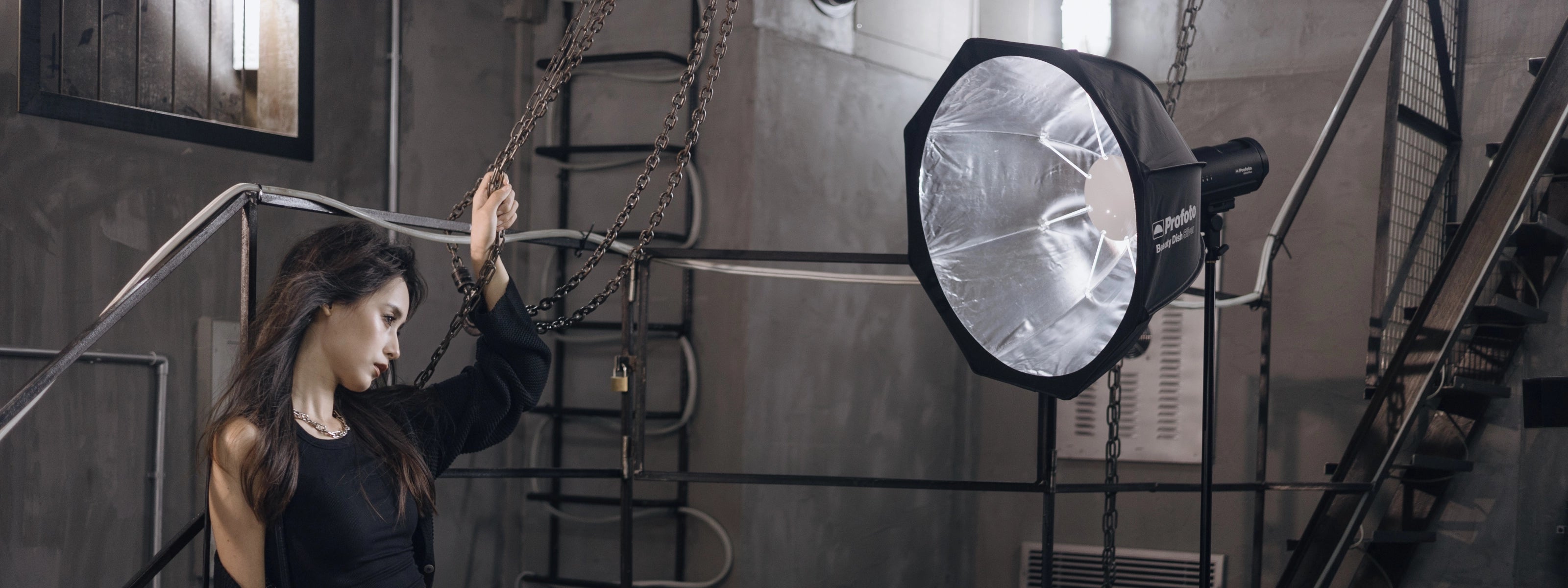 Model posing with chain with a Profoto Beauty Dish and light in an industrial setting. Product available at AJ's.
