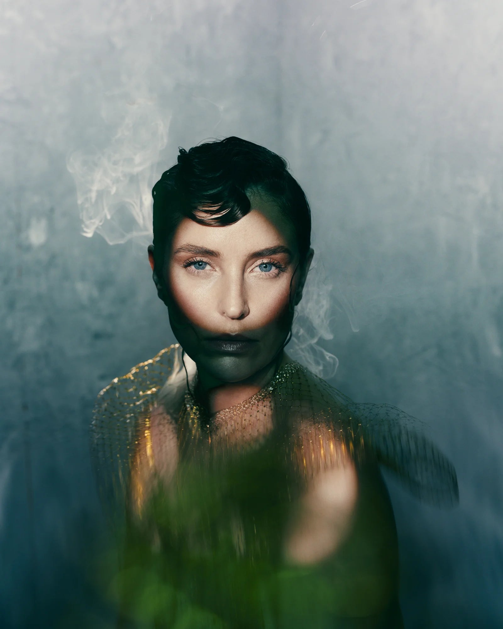 A colour photo of a model against a rough wall, with circle of light projected onto her face artistically.