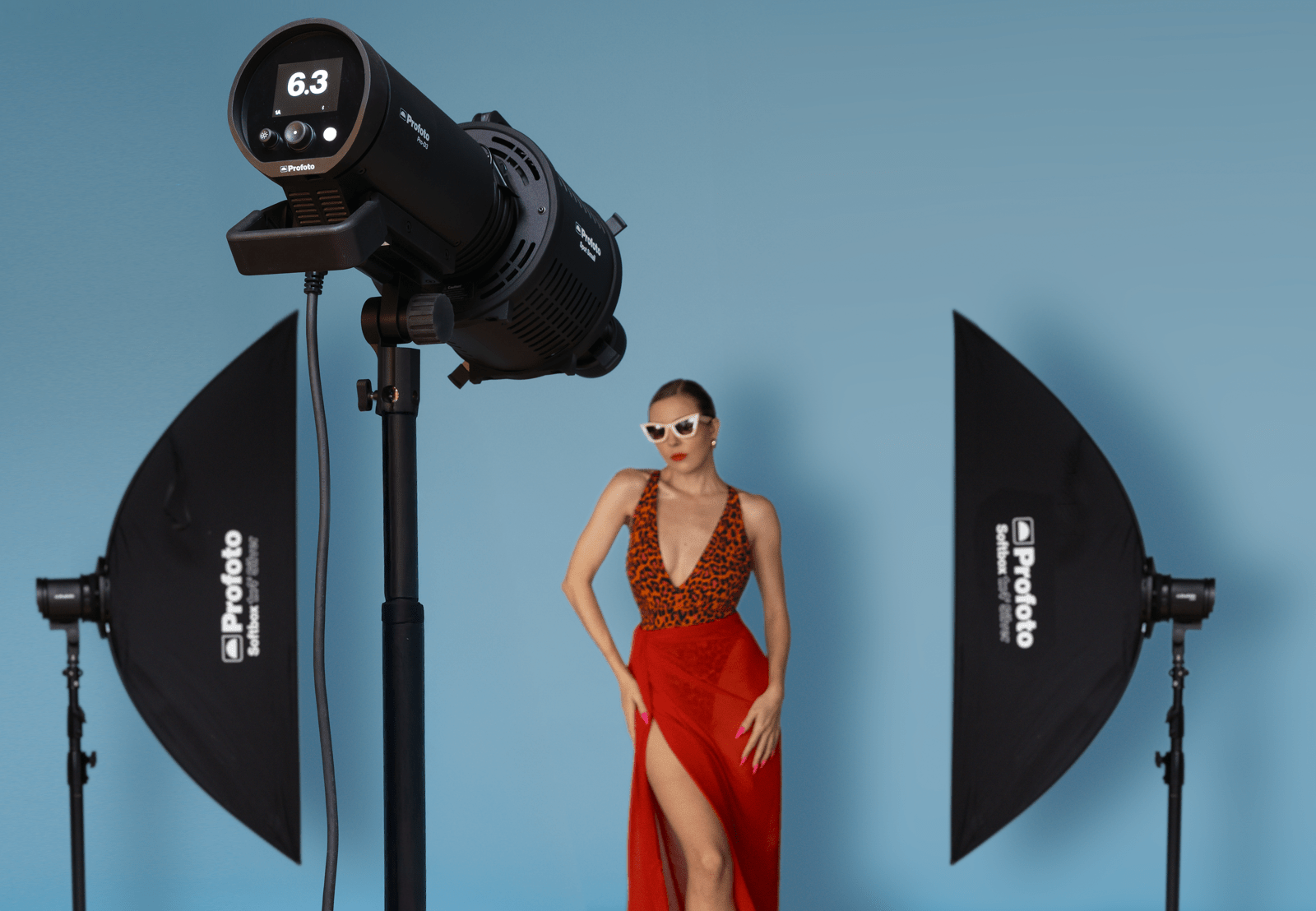 Female Model agains a blue background in a studio with profoto lights and small Profoto Spot in the foreground.