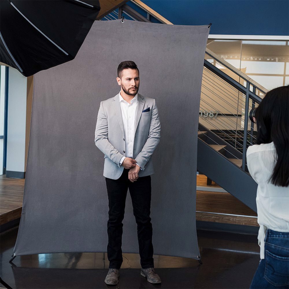 A smartly dressed man photographed against a grey fabric stretch background, shown in a modern rooftop scene. 