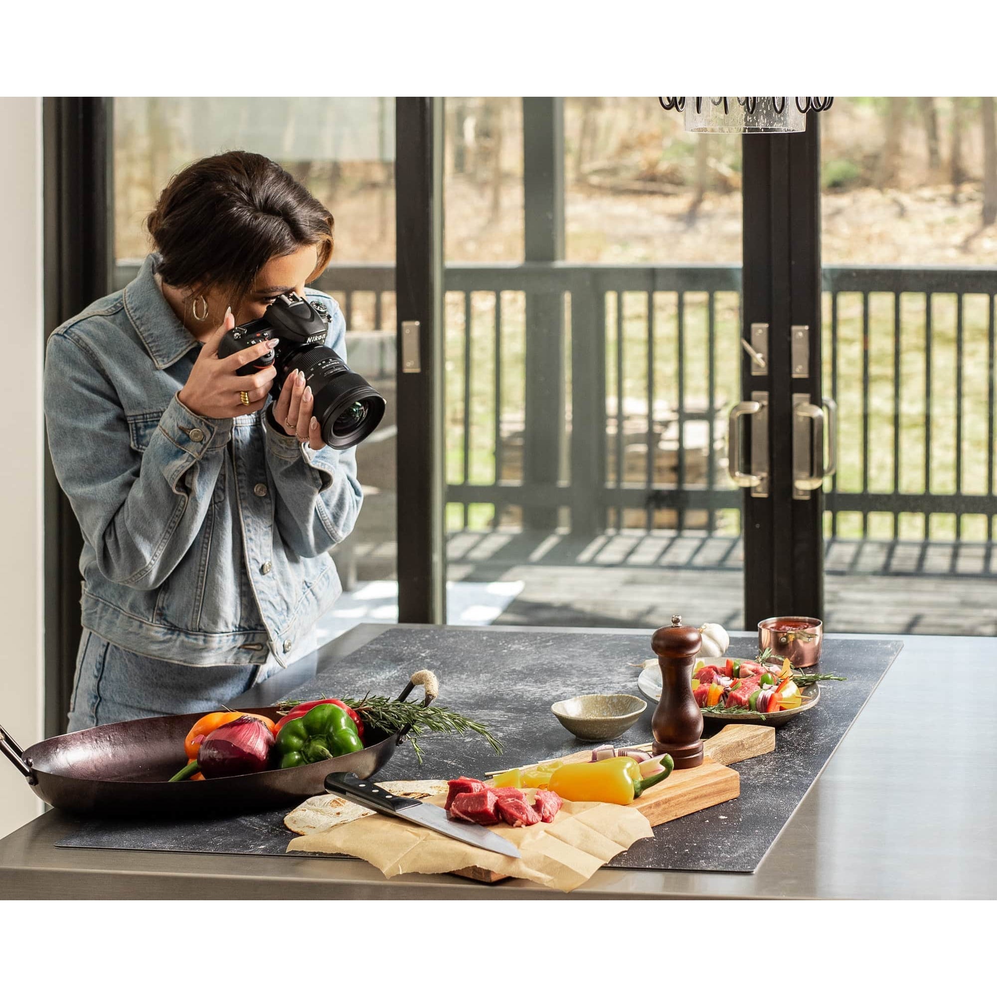 A female photographer capturing small items on a kitchen tabletop utilising the V-Flat Grey Chalk/Dark Chalk - XL Duo Board. 